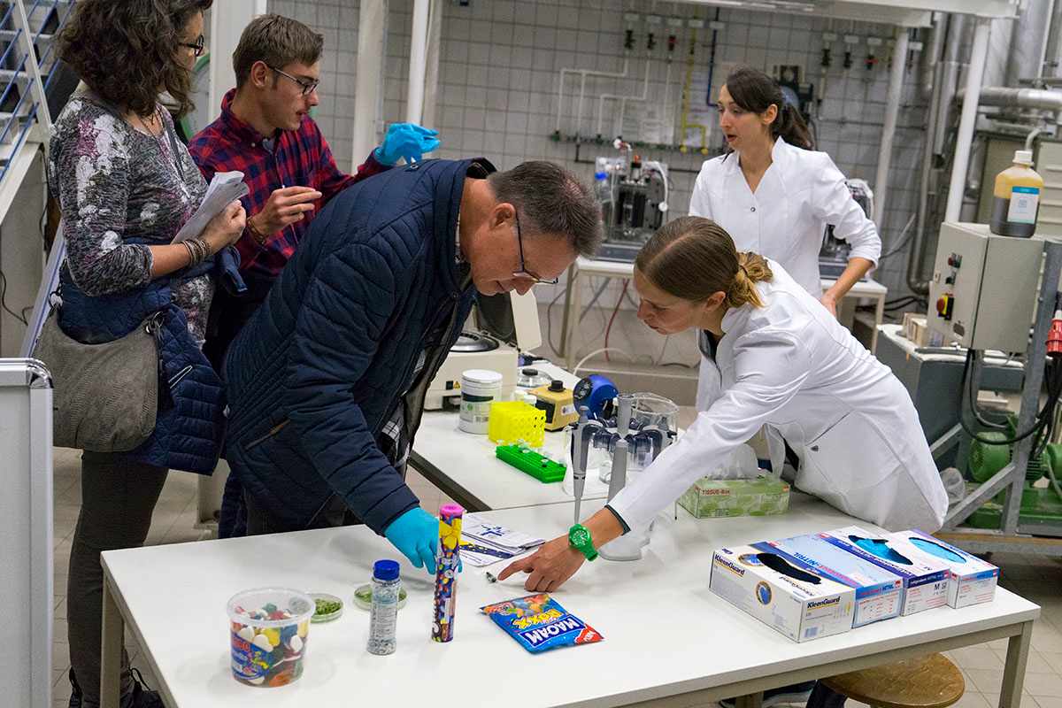 Eine Besucherin und zwei Besucher tauschen sich mit zwei Forscherinnen im Labor aus.